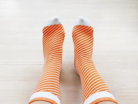 Feet wearing soft knitted patterned socks on a light wooden floor. Stock Photos