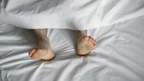 Feet on a white bed under a white blanket. Hand is scratching the leg. 4k 動画素材 106289231