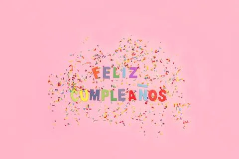 Feliz cumpleaños greeting with colored sprinkles on a pink background Stock Photos