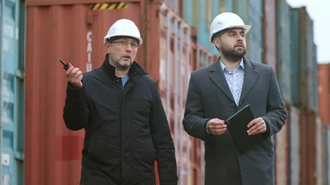 Fellow engineers walking and discussing in front of a stacked cargo container. A Stock Footage 306217367