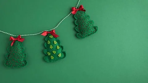 Felt christmas trees hanging on string against green background Stock Photos