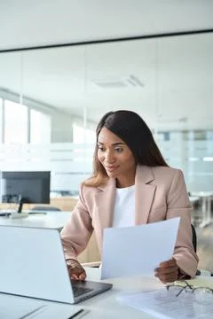 Female account manager checking document using laptop in office, vertical. Stock Photos