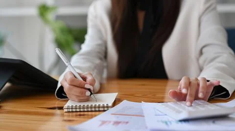 Female accountant making notes on notebook and using calculator at office desk. 스톡 사진
