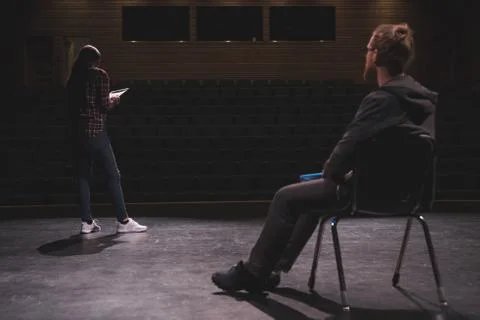 Female actress reading script while male actor looking at her on stage Stock Photos