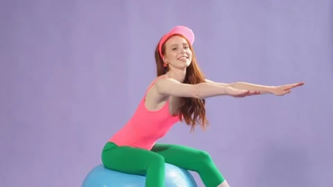 Female aerobics trainer in perfect shape sits on fitness ball with hands forward Stock Footage