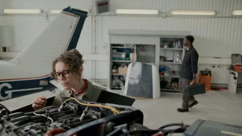 Female Aircraft Technician Checking Engine Parts and Writing Notes in Hangar Stock Footage 310849868