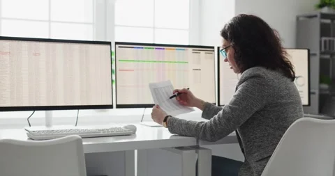 Female analyst auditing spreadsheets on three monitors in modern bright office Stock Footage 332068486