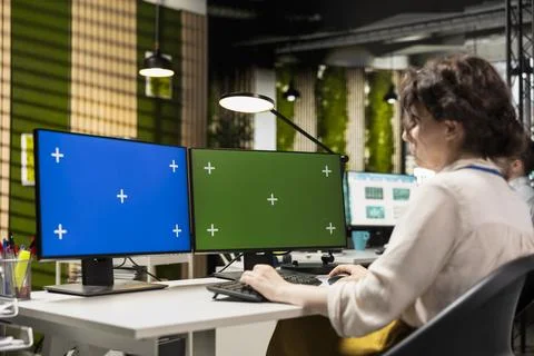 Female analyst uses computer monitors to analyze charts with chroma key Stock Photos