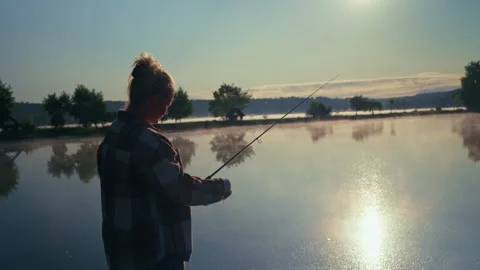 Female angler casting a spinning rod across a calm lake at sunrise Vidéo 340949188