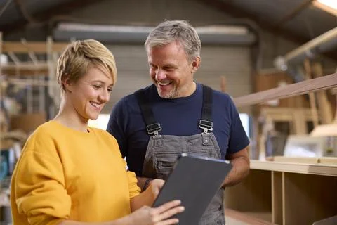 Female Apprentice With Digital Tablet Learning From Mature Male Carpenter In Stock Photos