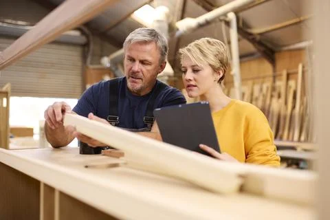 Female Apprentice With Digital Tablet Learning From Mature Male Carpenter In Stock Photos