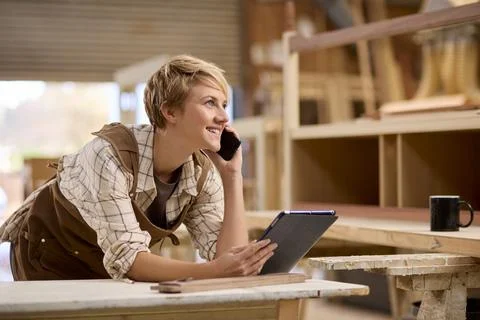 Female Apprentice With Digital Tablet Working As Carpenter In Furniture Workshop Stock Photos