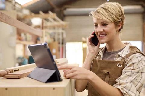 Female Apprentice With Digital Tablet Working As Carpenter In Furniture Workshop Stock Photos
