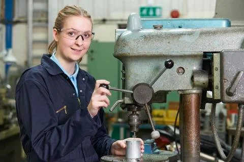 Female Apprentice Engineer Using Drill In Factory Foto stock