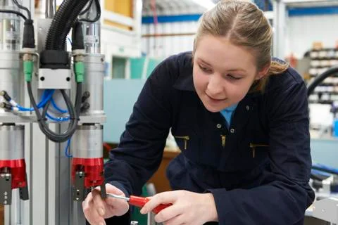 Female Apprentice Engineer Working On Machine In Factory Stock Photos