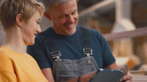 Female Apprentice Learning From Mature Male Carpenter With Digital Tablet In Stock Footage 242275645