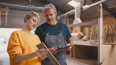 Female Apprentice Learning From Mature Male Carpenter With Digital Tablet In Stock Footage 242289458