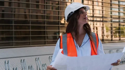Female architect checking blueprint at a modern construction site Stock Footage 340196035