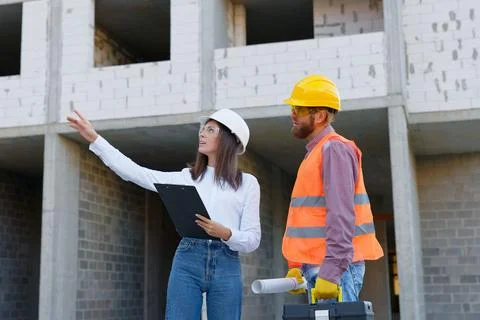 Female architect pointing at something while discussing with construction w.. Stock Photos