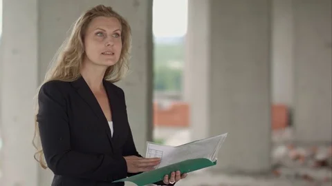 Female architect studying drafts while visiting large construction site Stock Footage 82801258