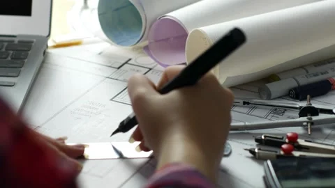 Female architect using laptop to reviewing blueprints and examining sketches at 库存影片 336573073