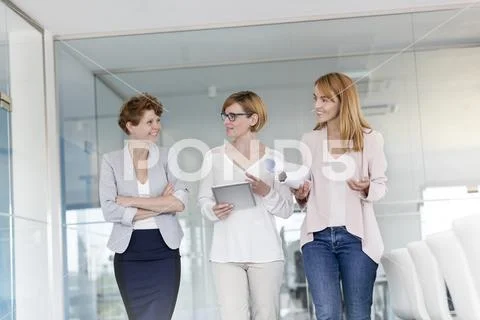 Female architects with digital tablet and blueprints walking and talking in Stock Photos