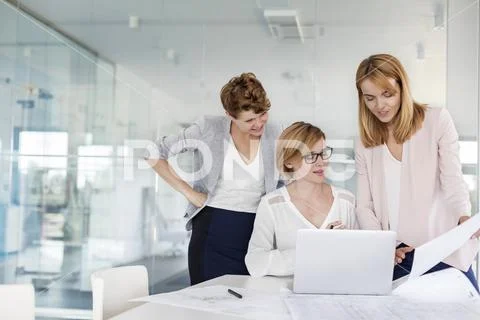 Female architects at laptop reviewing blueprints in conference room meeting Stock Photos