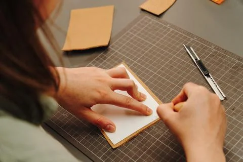 Female artisan aligns a paper pattern on leather at her workbench Stock Photos