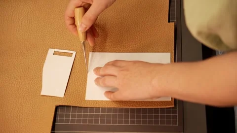 Female artisan cuts a paper pattern on natural leather at a workbench. Handmade Stock Footage 345969195