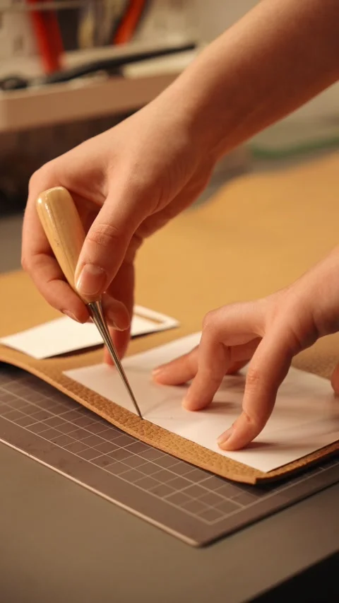 Female artisan cuts a paper pattern on natural leather at a workbench. Handmade Stock Footage 345970560