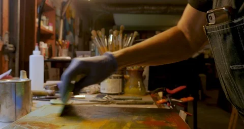Female artist using a silicone squeegee on a wooden panel while painting Stock Footage 120638564