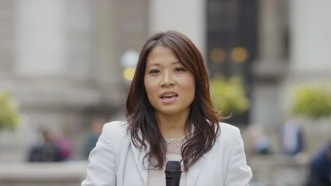 Female asian news reporter in the city reporting to camera Stock Footage