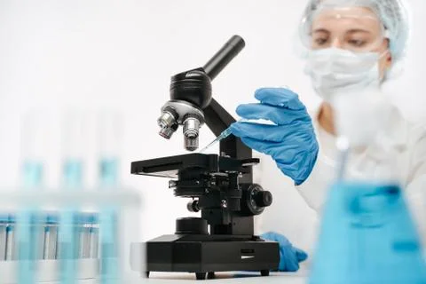 Female assistant working with microscope to make coronavirus test in clinic Stock Photos