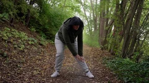 Female athlete bending down in forest setting, caucasian woman engages in warmup Video stock 321611673