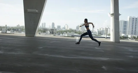 Female athlete leaping on top of an empty parking garage Stock Footage 99318324