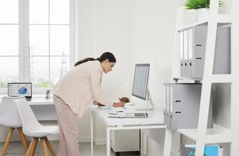 Female auditor analyzing paperwork at desktop computer in bright modern office Stock Photos