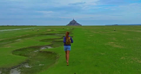 A female with a backpack visits the Mont Saint Michel castle while walking Stock Footage 302072847