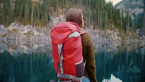 Female backpacke in green mountain pine woods lake is observing virgin nature Stock Footage 104047848