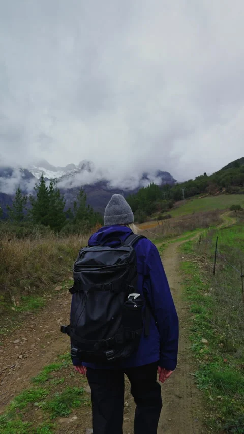Female backpacker hiking through rugged mountain terrain in cloudy weather Video stock 336623122