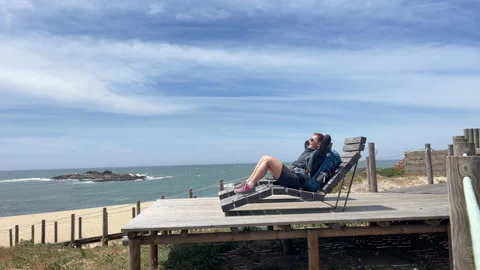 Female backpacker lying and sunbathing on Atlantic ocean rocky coast in Spain du Stock Footage 311083724