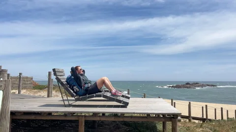 Female backpacker lying and sunbathing on Atlantic ocean rocky coast in Spain du Video stock 321844369