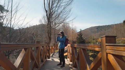 Female backpacker standing on a bridge on a mountain terrain and taking pictures Video stock 126531355