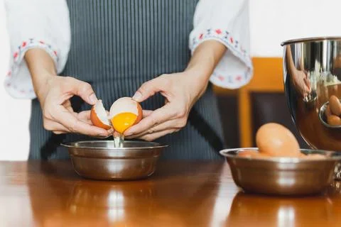 Female baker with apron cracking an egg prepare for baking on wooden table Stock Photos