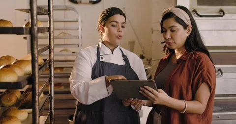 Female baker in coat and manager consulting tablet checking orders after manager Stock Footage 342113968
