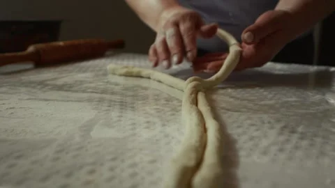Female baker skillfully twists and shapes dough into a braided form on a Stock Footage 339286451