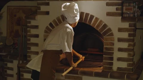 Female baker takes in bread in not yet heated stone oven preparing for hard Stock Footage 279231432