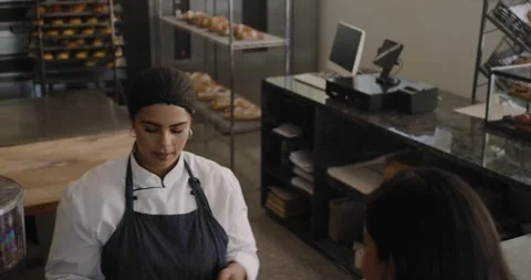 Female baker tapping tablet selecting pastry as customer with phone arriving to Video stock 345066037