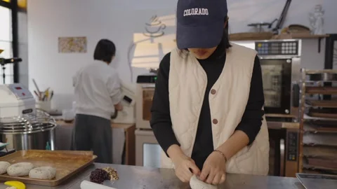 Female baker wearing cap skillfully stuffing and rolling dough on a stainless Stock Footage 328991949
