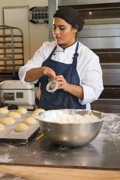 Female baker wearing chef jacket and apron measuring ingredient over dough at Stock Photos