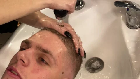 Female barber washes a young man's hair Stock Footage 337636635